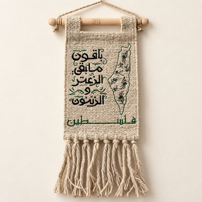 Handmade Palestinian burlap wall hanging with black Arabic embroidery, green Palestine map and olive branches, wooden hanger, and natural tassels on an ivory background.