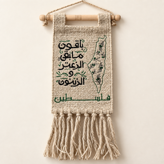 Handmade Palestinian burlap wall hanging with black Arabic embroidery, green Palestine map and olive branches, wooden hanger, and natural tassels on an ivory background.